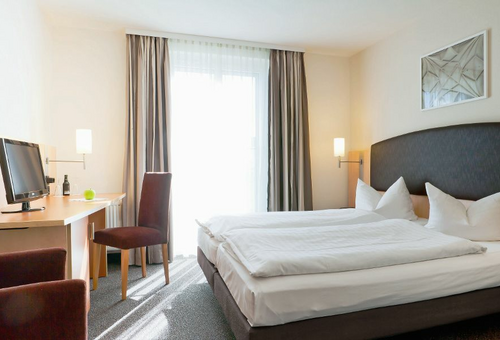 Helles Hotelzimmer mit Doppelbett, Schreibtisch und Stuhl.